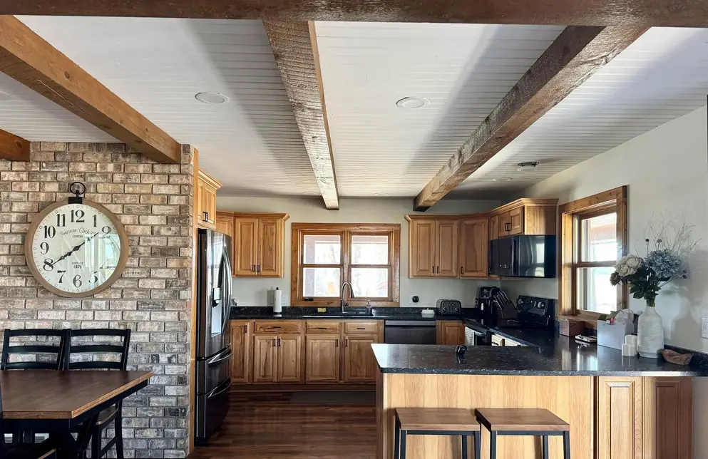 Kitchen with timber beams, a brick wall and honey-toned cabinets