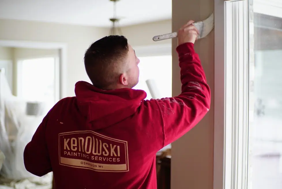 A painter in a Kenowski Painting hoodie brushing paint onto a wall