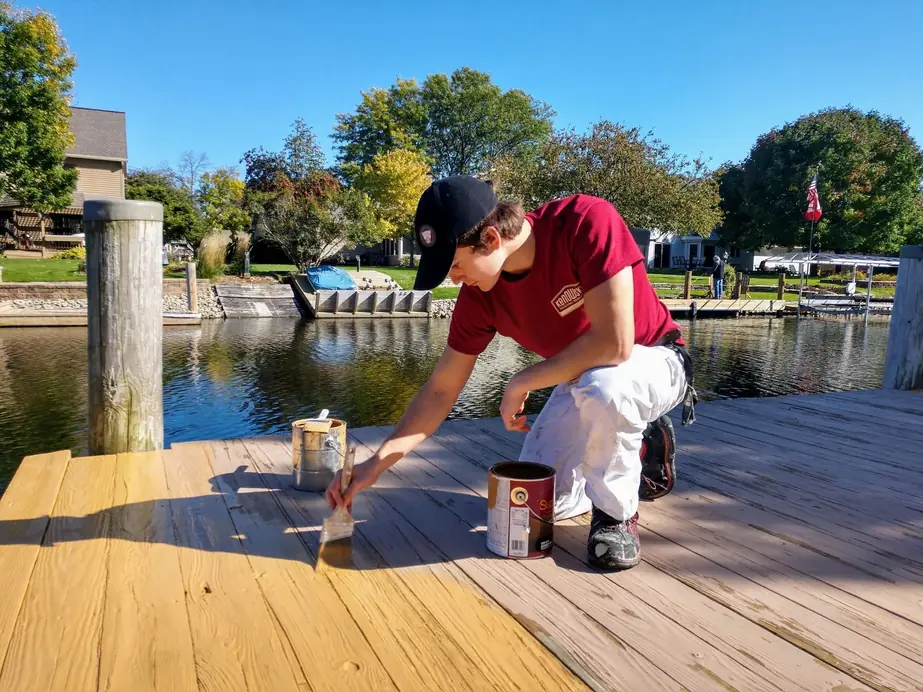 A Kenowski painter staining a lakeside deck in the sun